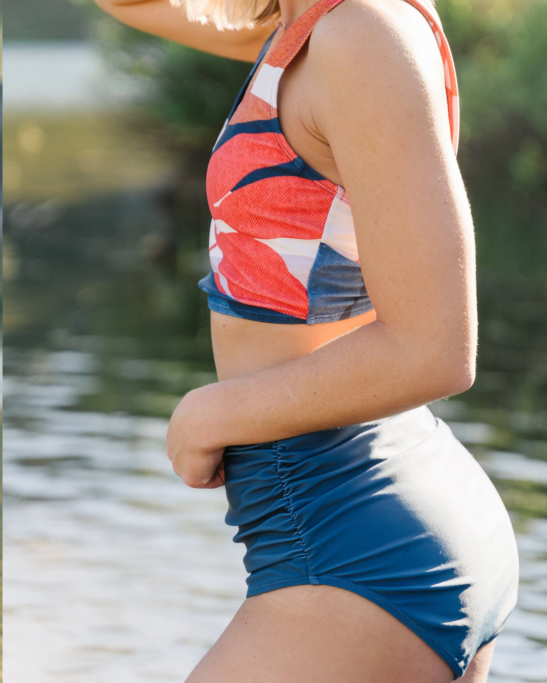 A women at the lake wearing blue high waisted ruched swimsuit bottoms.