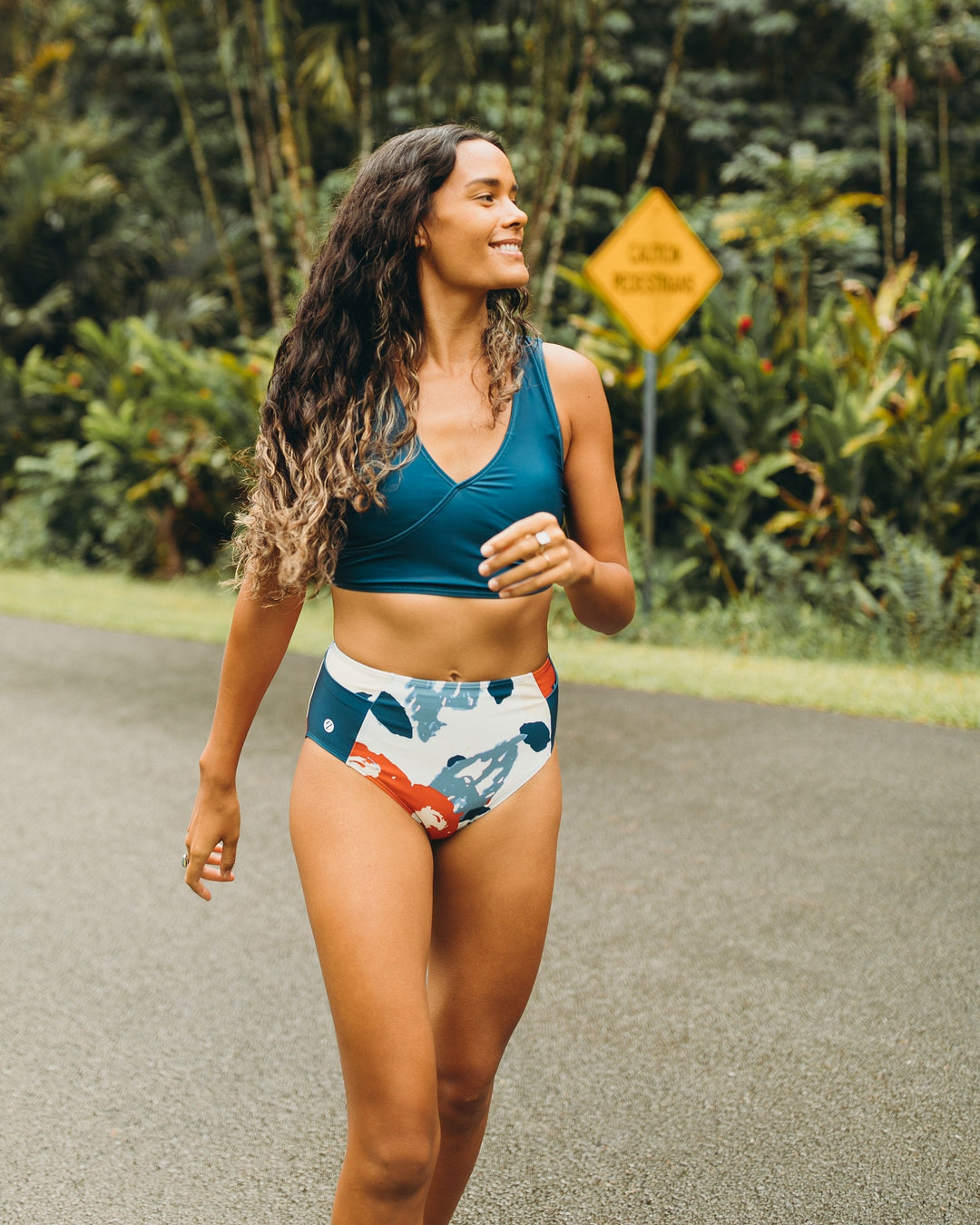 A women walking down the road in a red, white, and blue high waisted swimsuit bottom with a yoga pocket detail.