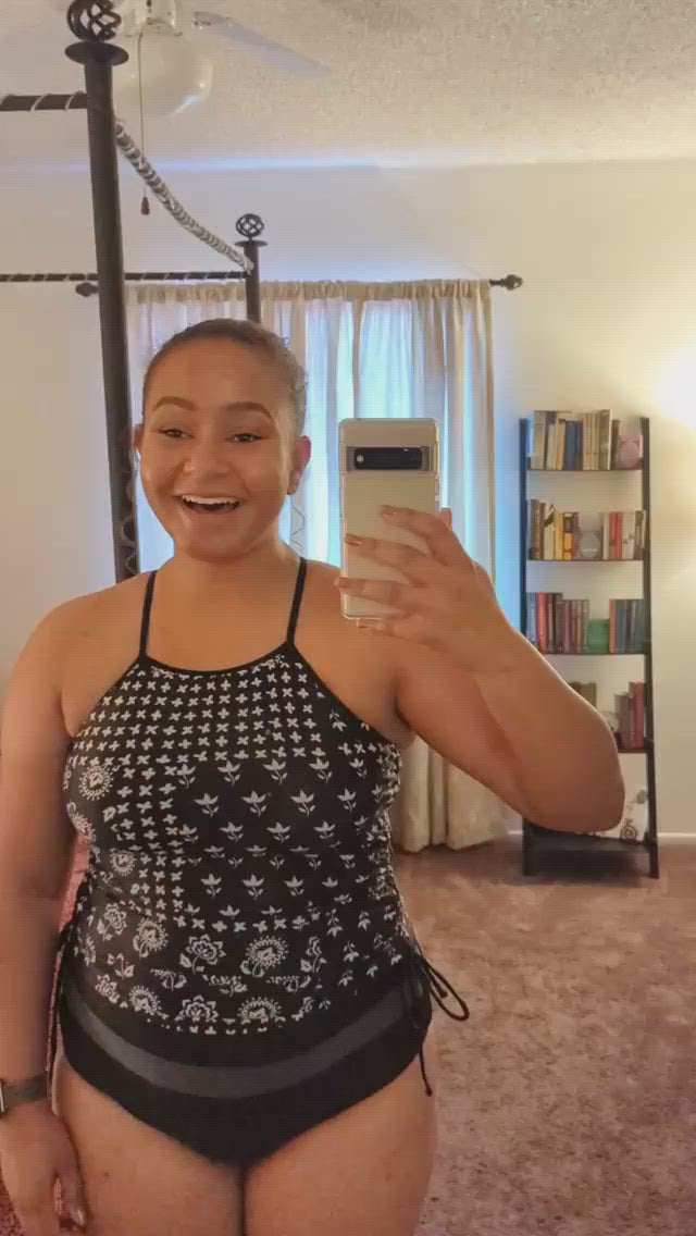 Video of a women filming herself in the mirror wearing a black and white floral tankini and talking about how it fits her.