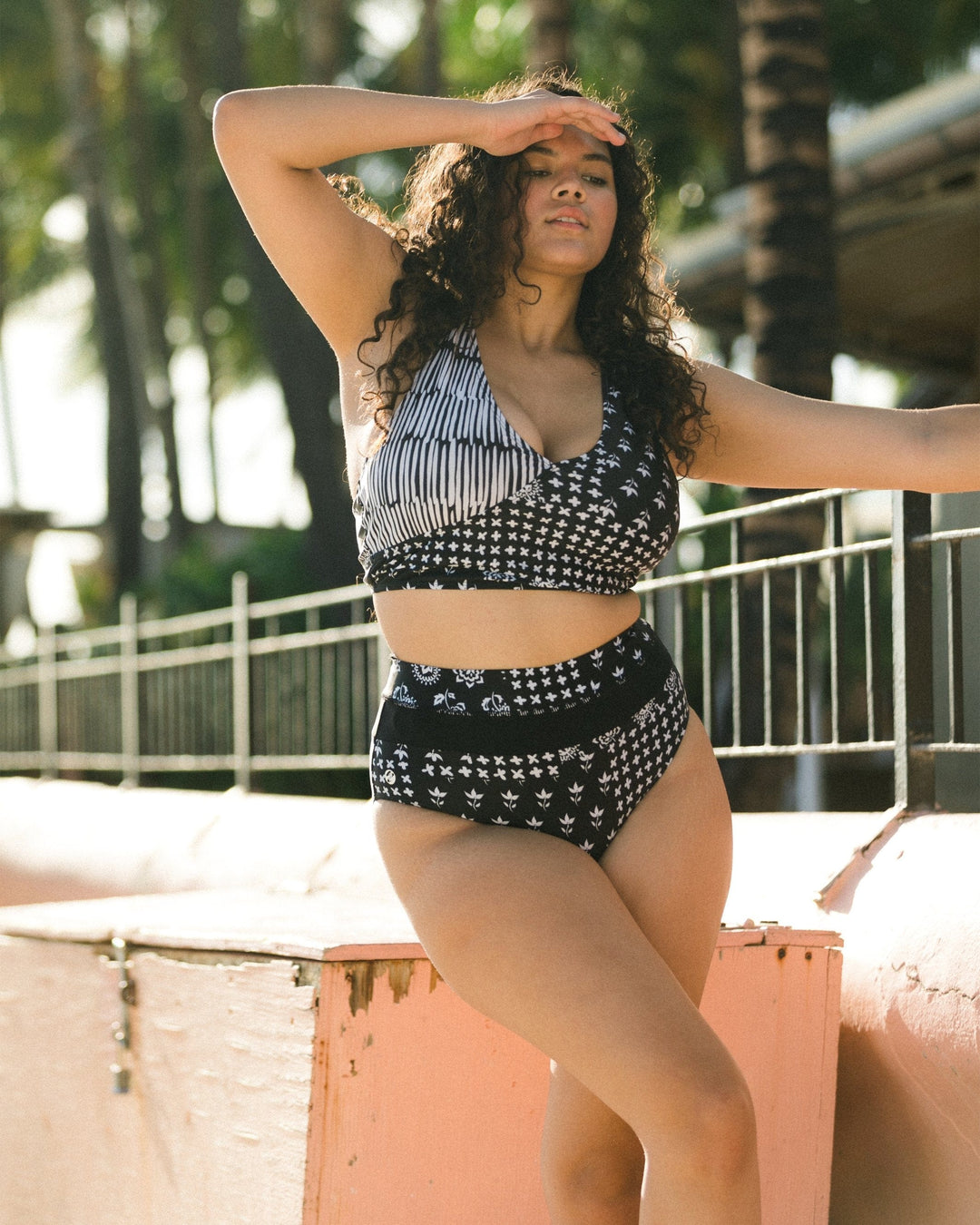 Young women with curly brown hair wearing a black and white floral two piece swimsuit. 