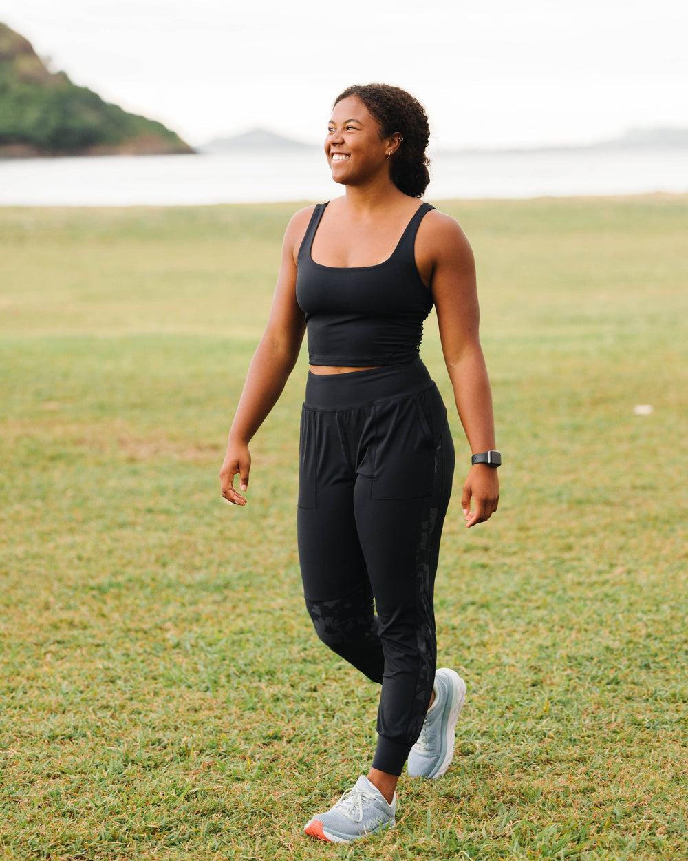 A happy young women wearing black exercise joggers with a grey and black floral pattern detail running down the side of the leg.