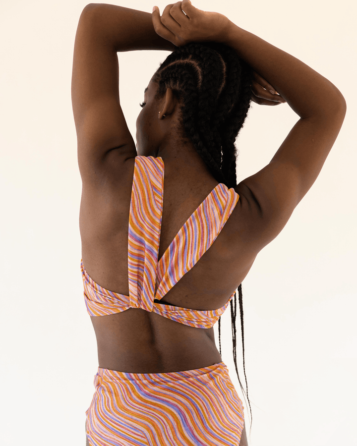 Back View studio picture of a girl wearing a retro pink, blue, purple and orange wave bikini top