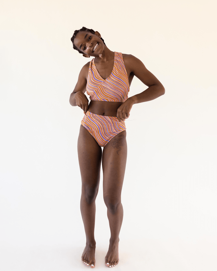 Full body studio picture of a girl wearing a retro pink, blue, purple and orange wave bikini top