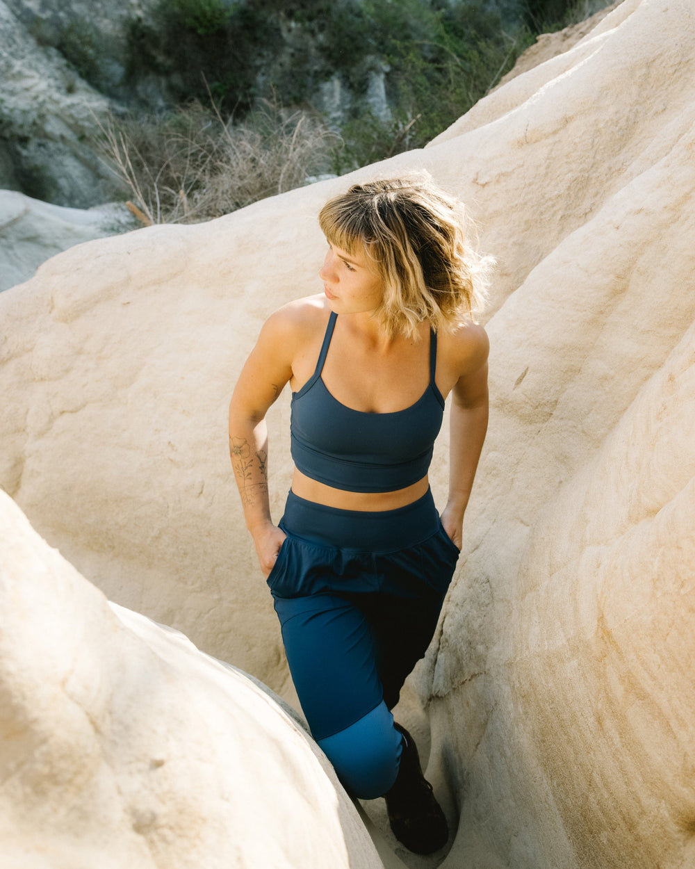 A women on a hike wearing dark blue joggers with a light blue panel detail running down the side of the leg and a light blue patch on the knee.